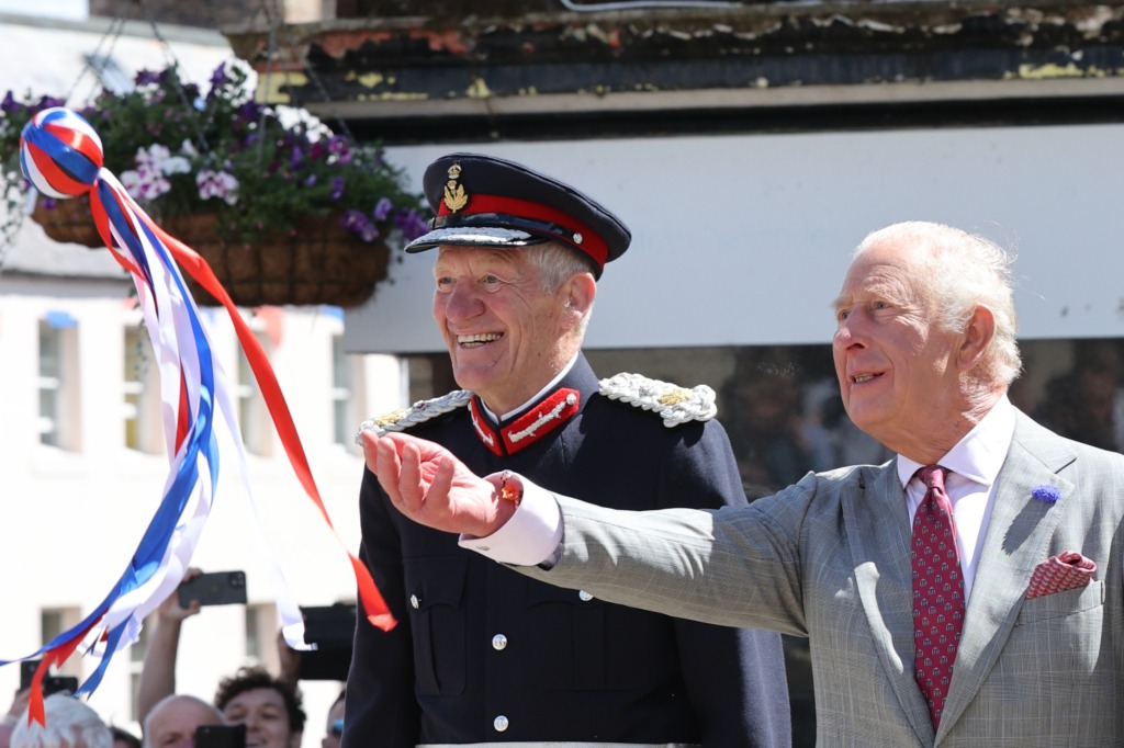Two elderly men in a parade; a uniformed officer with a red-trimmed hat and a gray-suited man waving colorful ribbons.