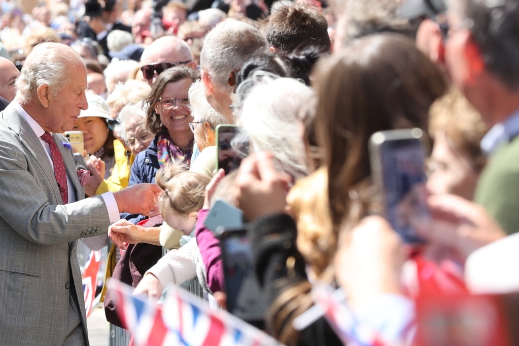 A man in a grey suit hands something to fans behind a barrier at an outdoor event, with many people reaching out.