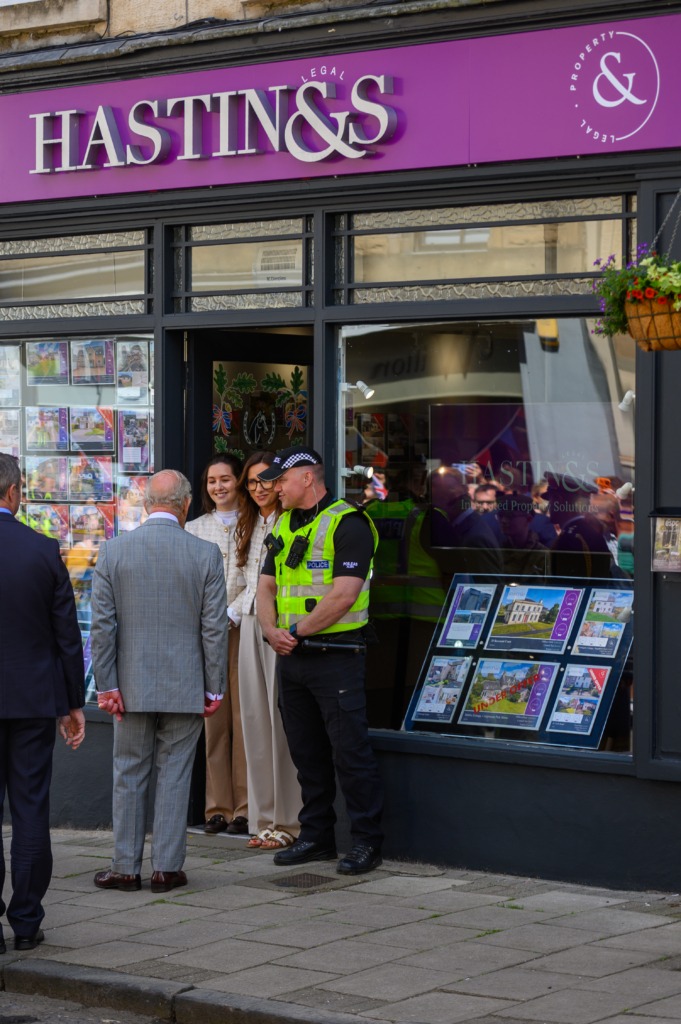 Group of people standing outside a purple Hastings & Co storefront, chatting near a police officer in a high-visibility vest.
